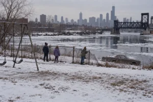 Children stand behind a fence overlooking ice-covered water on a snowy day.